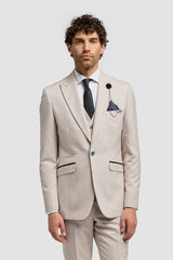 Vīrietis bēšā uzvalkā ar baltu kreklu un brūnām kurpēm uz gaiši pelēka fona